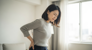 ぎっくり腰で腰を押さえてつらそうにする30代の日本人女性
