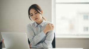 デスクワーク中に肩を押さえて疲れた表情を見せる30代日本人女性