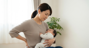 産後の腰痛に悩みながら赤ちゃんを抱く30代の日本人女性